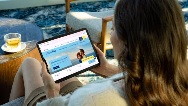 Tui Cruises, Frau schaut online am Tablet nach einer neuen Kreuzfahrt