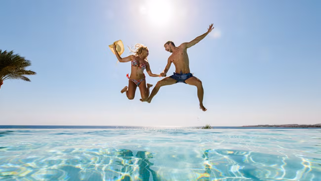 Fröhliches Paar springt in Pool und hat Spaß dabei, Adults Only Urlaub