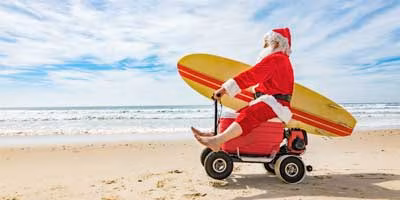 Weihnachtsmann mit Surfbrett am Strand