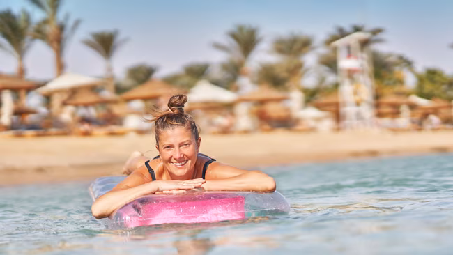 Ägypten - Hurghada, Frau auf aufblasbarer Matratze im kristallklaren Meer, Strand mit Liegen