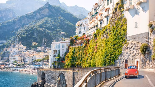 Italien - Amalfikueste, Bunte Häuse an Steinklippen mit rotem Olditimer Auto auf Straße