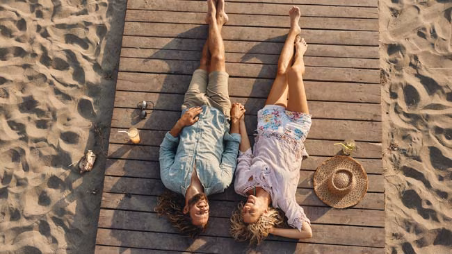 Glückliches Paar entspannt liegend am Steg am Strand mit Cocktails