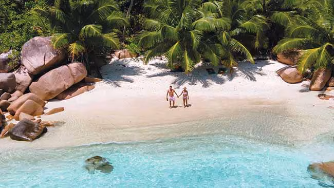 Indischer Ozean - Seychellen, Paar steht an Traumstrand mit kristallklarem Wasser und Palmen