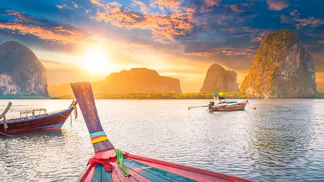 Thailand, Strand mit Booten & Felsen im Sonnenuntergang