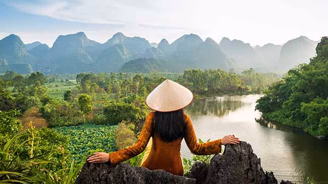 Vietnam, Frau am Fluss mit Bergen im Hintergrund