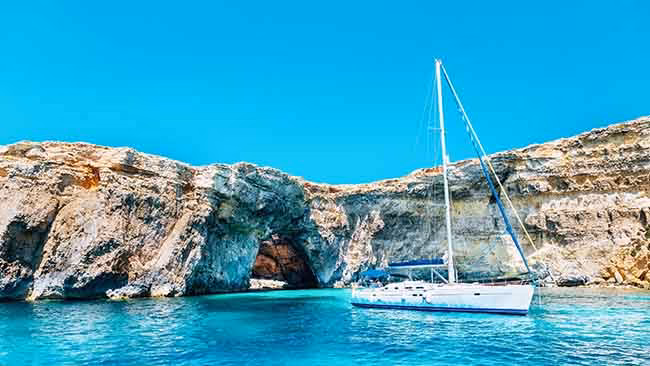 Malta, Schiff in Bucht mit kristallklarem Wasser und Felsen im Hintergrund