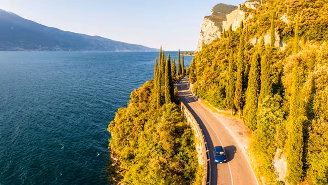 Italien - Gardasee, Auto fährt an sonniger Küstenstraße / Uferpromenade entlang