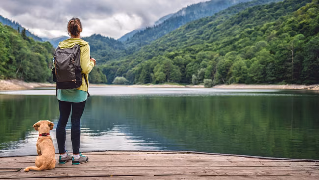 Frau steht mit Hund am Steg eines Sees, Wanderurlaub mit Hund