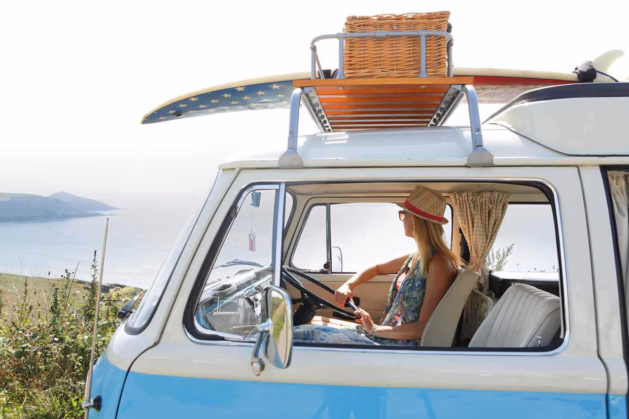 Camper Junge Frau im Bus mit Surfboard auf dem Dach