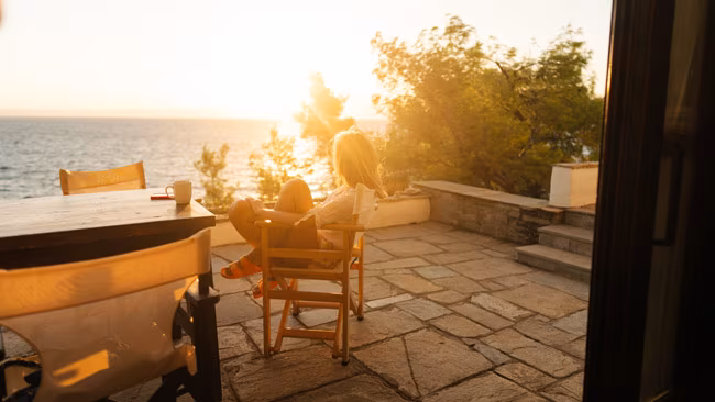 Frau genießt Morgen auf Terrasse in Ferienwohnung, Sonnenaufgang am Meer