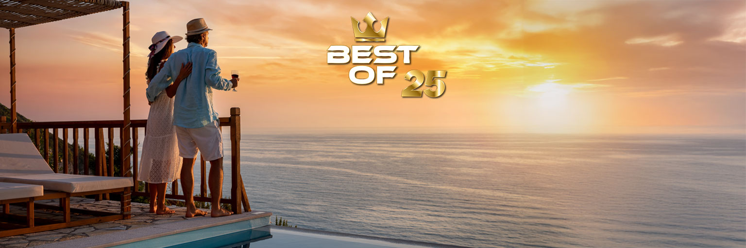 Paar mit Weinglas blickt bei Sonnenuntergang aufs Meer