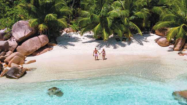 Indischer Ozean - Seychellen, Paar steht an Traumstrand mit kristallklarem Wasser und Palmen