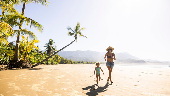 Costa Rica, Frau mit Tochter rennt unter Palmen am Strand entlang