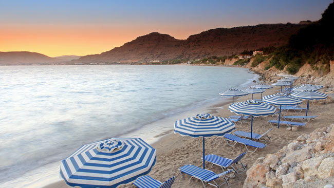 Pefkos Stand mit Liegen und Sonnenschirmen im Sonnenuntergang auf Rhodos, Griechenland