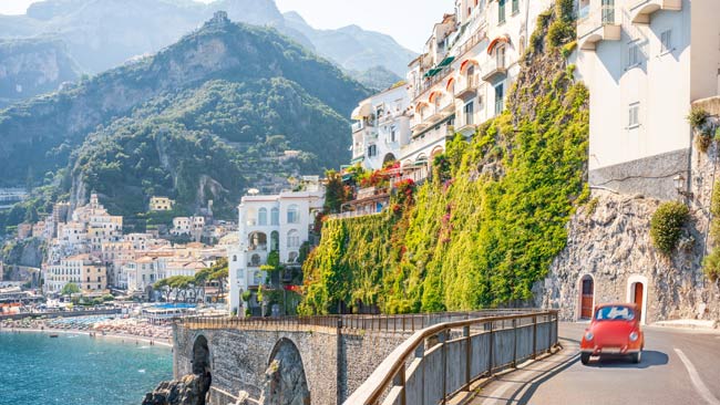Italien - Amalfikueste, Bunte Häuse an Steinklippen mit rotem Olditimer Auto auf Straße