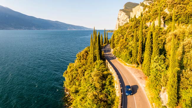 Italien - Gardasee, Auto fährt an sonniger Küstenstraße / Uferpromenade entlang