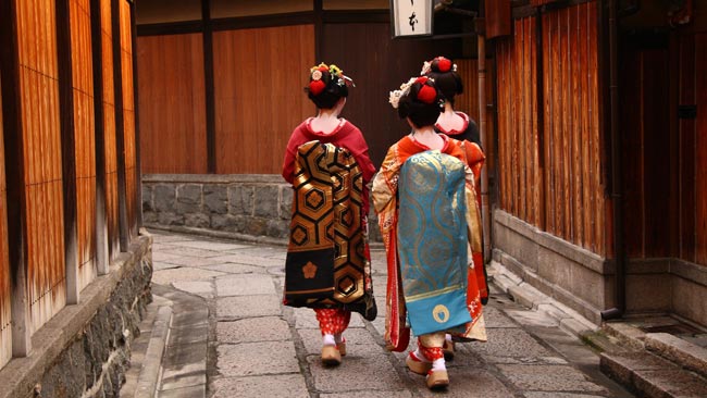 Drei Geisha laufen zwischen Holzhütten im Geishaviertel Gion, Japan