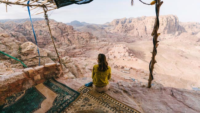Jordanien - Frau sitzt auf traditionellen Teppich in Petra und genießt Aussicht