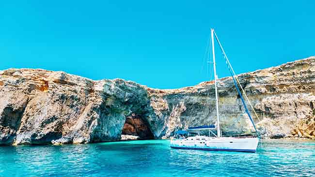 Malta, Schiff in Bucht mit kristallklarem Wasser und Felsen im Hintergrund