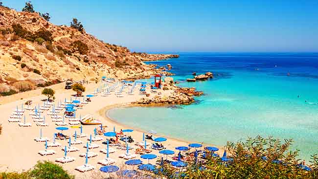 Zypern, Strand mit Sonnenschirmen und Liegen in einer Bucht