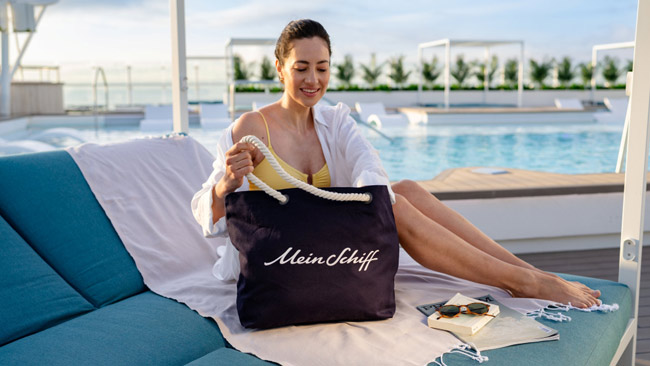 Mein Schiff Relax - Frau liegt am Pool mit Mein Schiff Tasche