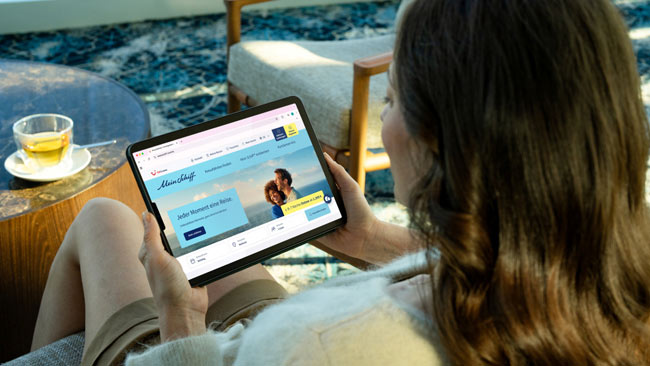 Tui Cruises, Frau schaut online am Tablet nach einer neuen Kreuzfahrt