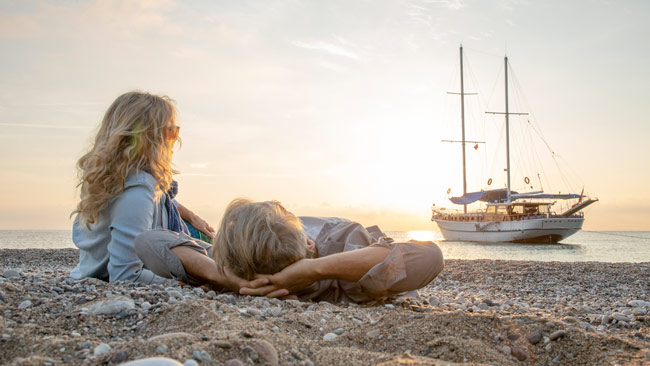 Älteres Paar entspannt am Strand und genießt Sonnenuntergang mit Blick auf Boot im Meer