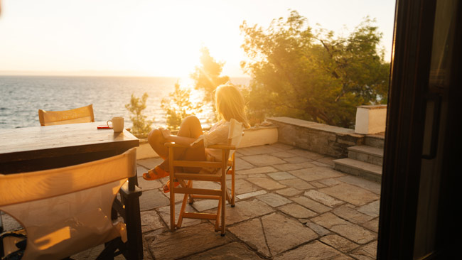 Frau genießt Morgen auf Terrasse in Ferienwohnung, Sonnenaufgang am Meer