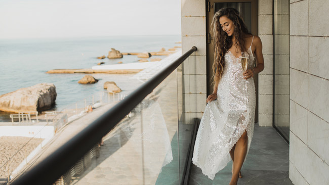 Frau in Glitzerkleid mit Champagnerglas auf Balkon, Adults Only Hotel