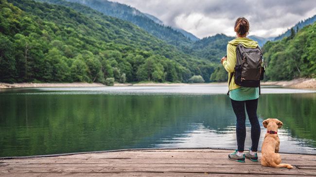 Frau steht mit Hund am Steg eines Sees, Wanderurlaub mit Hund