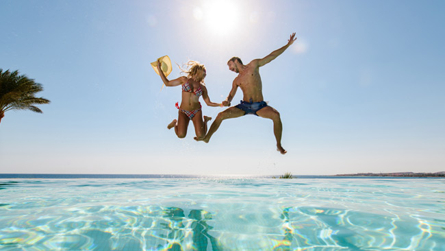 Fröhliches Paar springt in Pool und hat Spaß dabei, Adults Only Urlaub