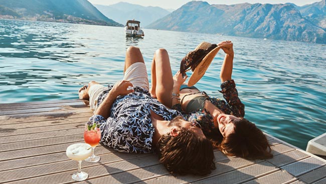 Glückliches Paar liegt am Steg eines Sees und genießt Cocktails