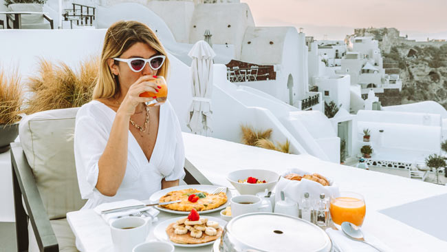 Griechenland - Santorini, Gedeckter Tisch, Frau beim Frühstück mit Aussicht auf Oia