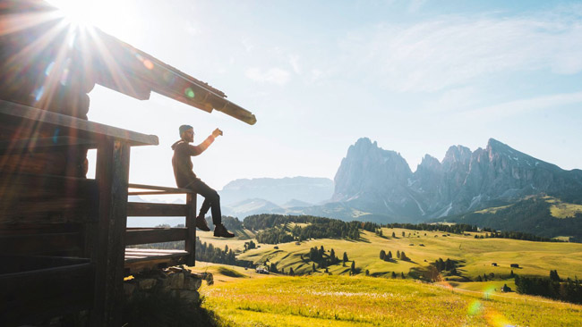 Junger Mann genießt Blick auf Berge von Berghütte oder Ferienhaus aus