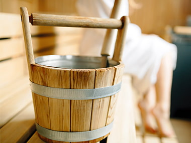 Eimer in der Sauna mit Dame im Hintergrund
